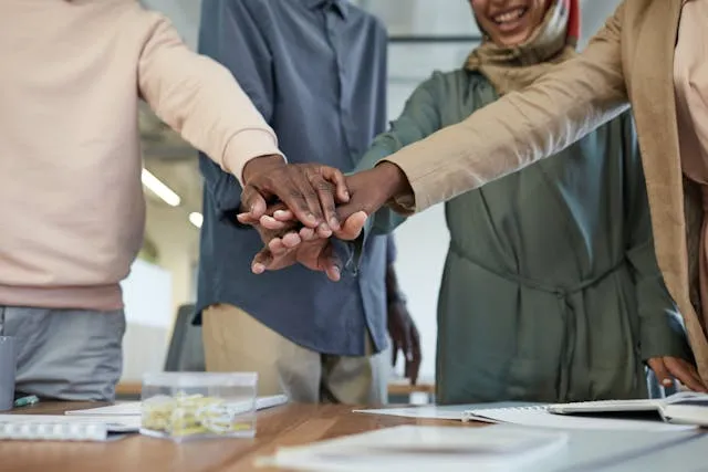 A team of individuals in an office, standing in a circle and holding hands, illustrating solidarity and cooperation.